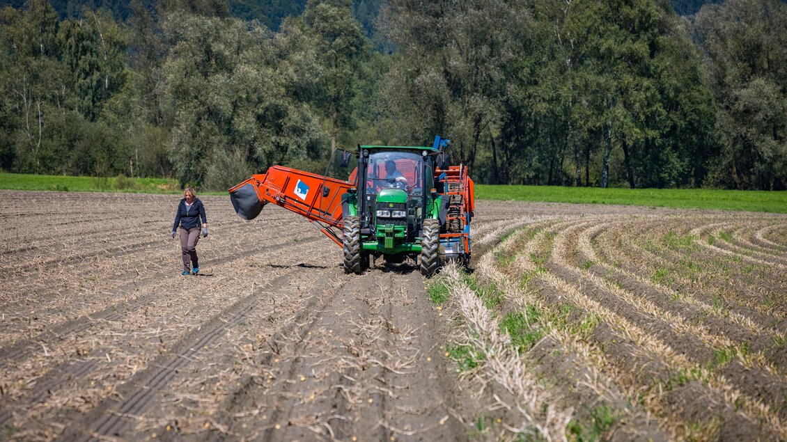 Ein Traktor bearbeitet ein Feld, während ein Landwirt in der Nähe arbeitet. Die Umgebung ist grün und von Bäumen umgeben. | © Netzwerk Kulinarik wildbild