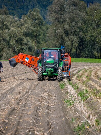 A tractor is cultivating a field while a farmer works nearby. The surroundings are green and surrounded by trees. | © Netzwerk Kulinarik wildbild
