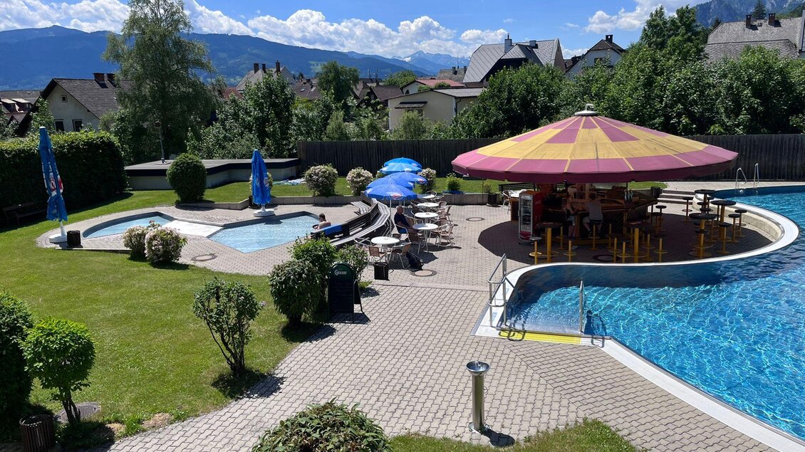 Ein schöner Außenpool mit Liegen und einem bunten Sonnenschirm. Die Umgebung ist grün und einladend, ideal für Entspannung. | © Marktgemeinde Stainach-Pürgg