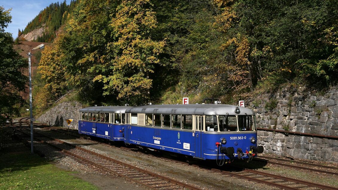 Ein blauer Schienenbus steht an einem Bahngleis, umgeben von herbstlichen Bäumen. Die Umgebung ist ruhig und ländlich. | © Thomas Schneider