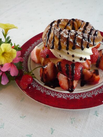 Ein Dessertteller mit frischen Erdbeeren, einer Waffel und einer Kugel Sahne, garniert mit Schokoladensauce. Daneben eine kleine Blume, die das Bild verschönert. | © Eschachalm
