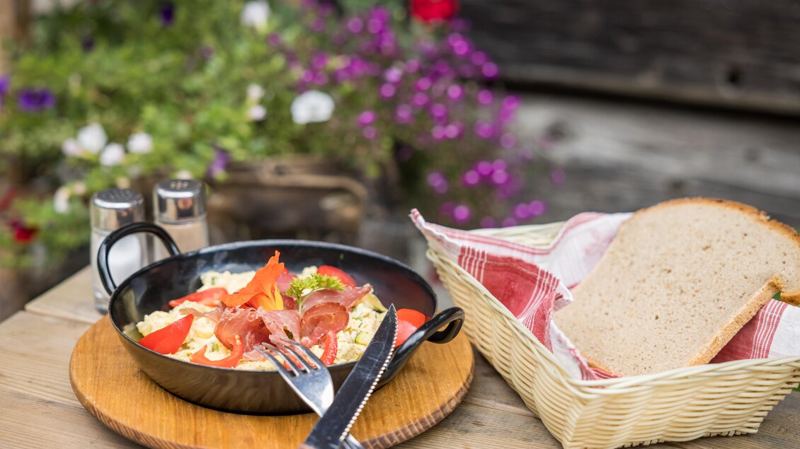 Ein Teller mit einer bunten Mischung aus Gemüse, Schinken und Kräutern, serviert in einer Pfanne. Daneben liegt ein Stück frisches Brot und eine Korb mit mehr Brot. | © Netzwerk Kulinarik wildbild