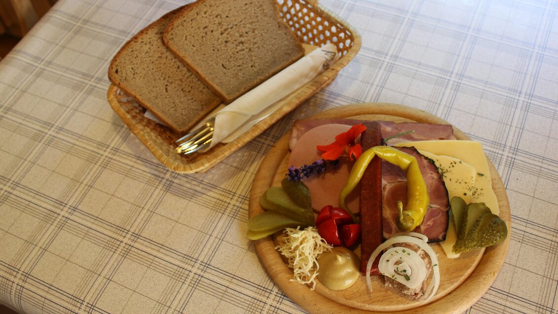 Ein Holzbrett mit einer Auswahl an Wurst, Käse und eingelegtem Gemüse. Daneben liegt ein Korb mit frischem Brot. | © Eschachalm