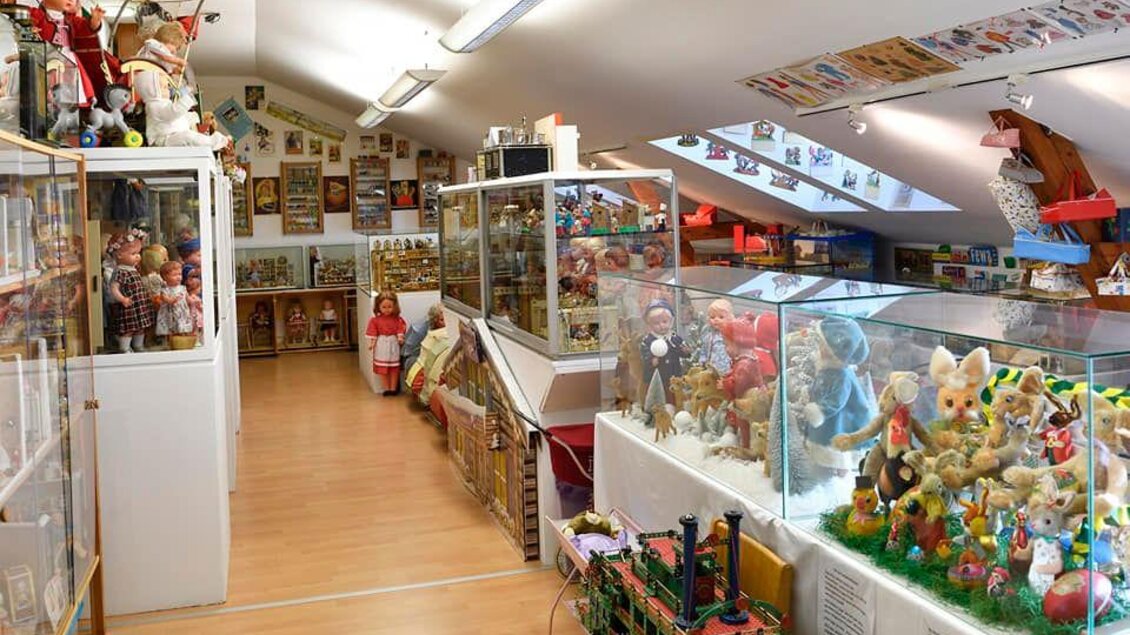 Ein gemütlicher Ausstellungsraum mit vielen Schaufensterauslagen. Die Wände sind mit alten Spielzeugen und Puppen dekoriert. | © Eva Kohlbacher