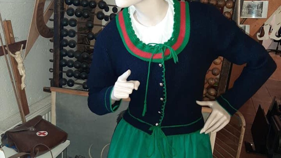 Eine Schaufensterpuppe in traditioneller Kleidung steht in einem Raum. Sie trägt ein blaues Oberteil mit roten und grünen Akzenten sowie einen grünen Rock. | © Eva Kohlbacher