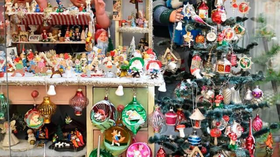 Ein dekorierter Weihnachtsbaum mit bunten Ornamenten steht neben einer Vitrine mit Spielzeugen und Puppen. Die Szene vermittelt festliche Stimmung und Nostalgie. | © Eva Kohlbacher