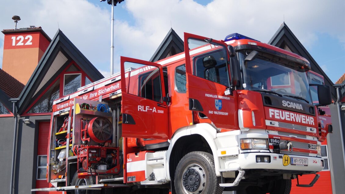 Ein rotes Feuerwehrauto steht vor einer Feuerwache. Im Hintergrund sind die Gebäude und ein blauer Himmel zu sehen. | © FF Bad Walterdorf