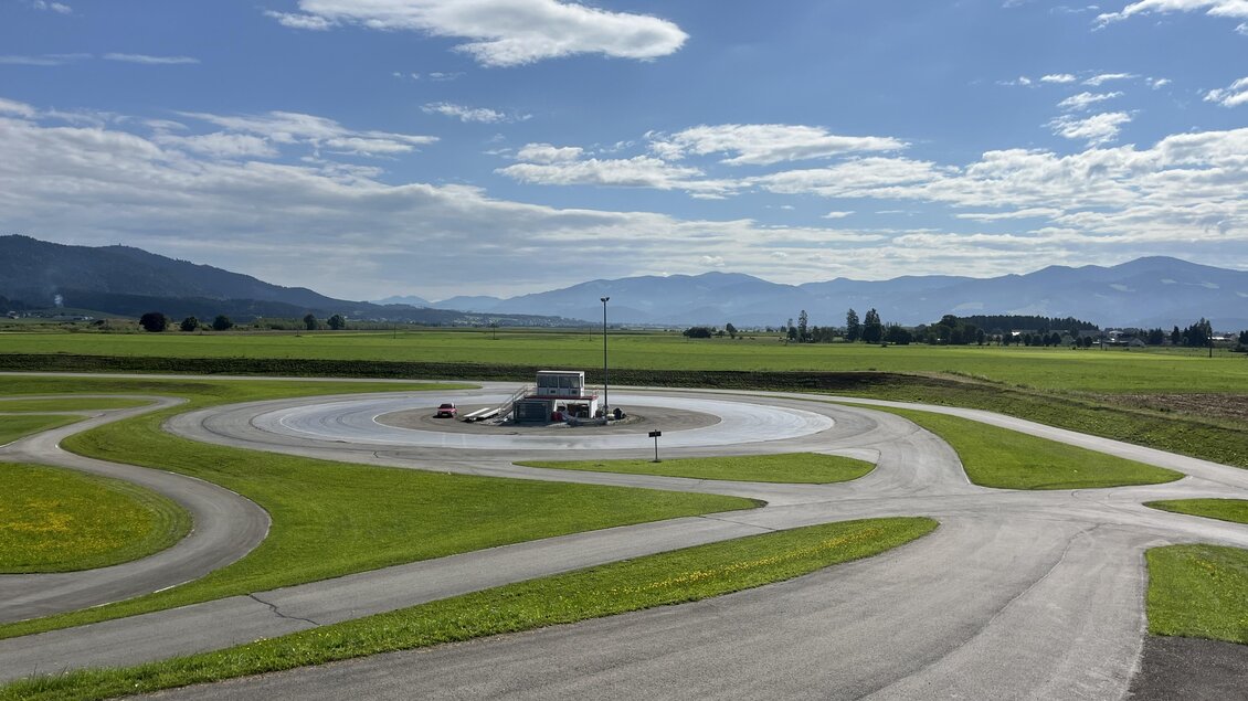 Eine weitläufige Landschaft mit einer Kurvenbahn und sanften Hügeln im Hintergrund. Der Himmel ist klar und blau mit einigen Wolken. | © Peter Hopf