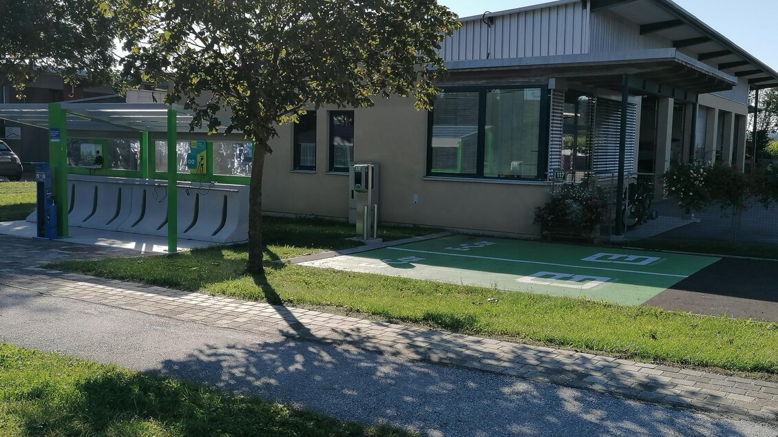 Ein modernes Gebäude mit großen Fenstern und einem begrünten Außenbereich. Auf der linken Seite befindet sich eine Fahrradstation. | © Thermen- & Vulkanland