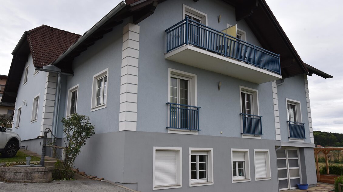 Ein modernes zweistöckiges Haus in sanften Blautönen. Es hat einen Balkon, große Fenster und befindet sich in einer ländlichen Umgebung. | © Glatz