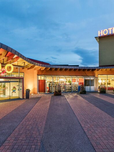 A modern hotel building with an inviting facade. The exterior view is well-lit and shows the entrance area with plants. | © TVB Bad Waltersdorf