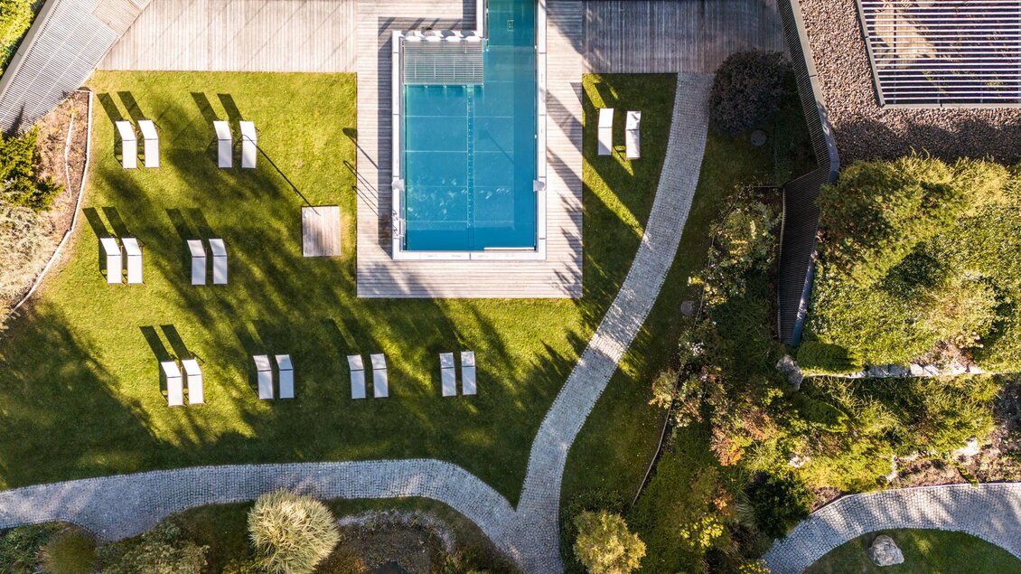 Ein stilvoller Garten mit einem Swimmingpool und modernen Liegen. Sanfte Wege und grüne Pflanzen sorgen für eine entspannte Atmosphäre. | © Falkensteiner Hotel Schladming/ Fotograf Dragan Dokmanovic