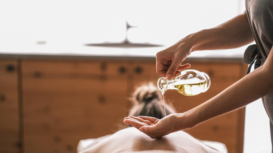 Eine Person erhält eine Massage, während das Massageöl auf die Handfläche gegossen wird. Der Raum ist hell und entspannend gestaltet. | © Falkensteiner Hotel Schladming/ Fotograf Dragan Dokmanovic