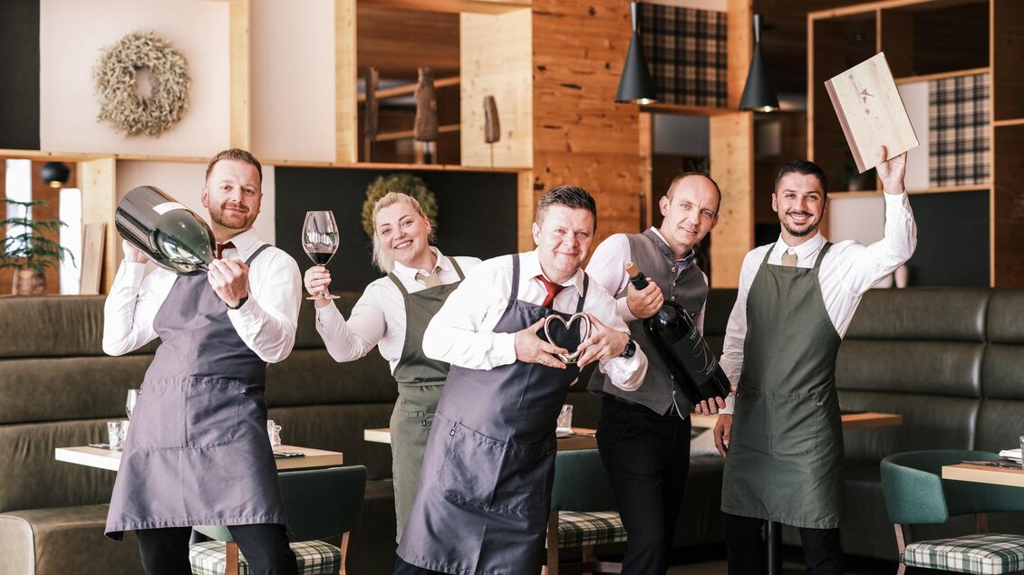 Ein fröhliches Team von Kellnern in einem eleganten Restaurant. Sie halten verschiedene Utensilien und haben gute Laune. | © Falkensteiner Hotel Schladming/ Fotograf Dragan Dokmanovic