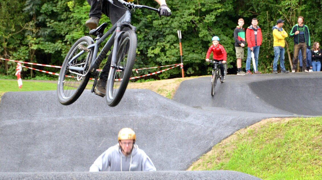Ein Fahrer springt mit seinem Mountainbike über eine Rampe. Im Hintergrund stehen Zuschauer, die das Ereignis beobachten. | © Gemeinde Ligist-Kremser Gottfried