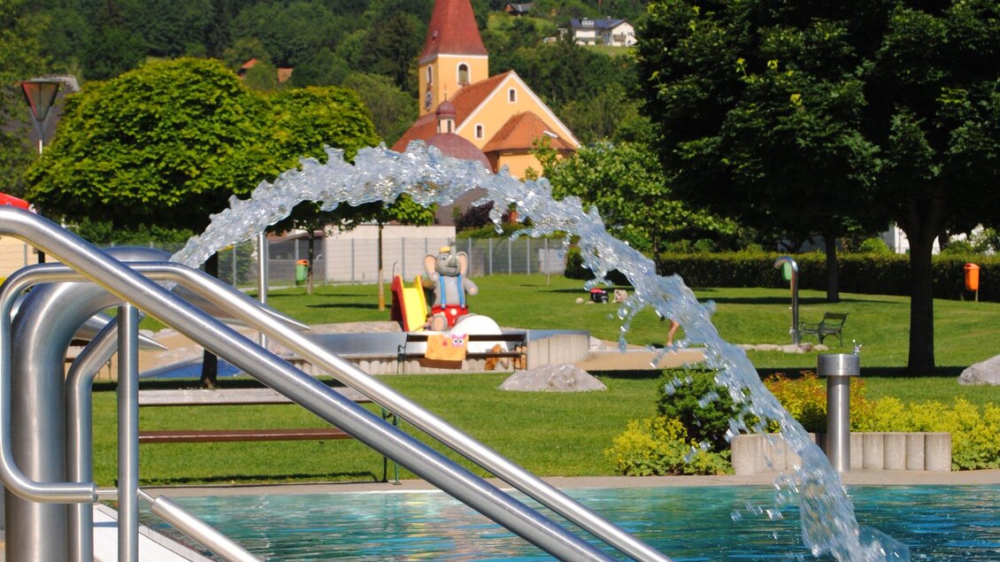 Ein schöner Garten mit einem Pool und einem Wasserspiel. Im Hintergrund sind grüne Bäume und eine kleine Kirche zu sehen. | © Marktgemeinde Ligist