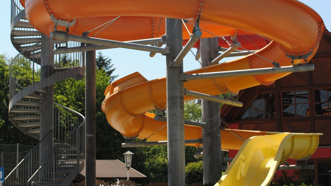 Eine Wasserrutsche in einem Freizeitpark mit einer spiralförmigen Treppe. Die Rutsche ist orange und gelb und bietet Spaß für alle Altersgruppen. | © Marktgemeinde Ligist