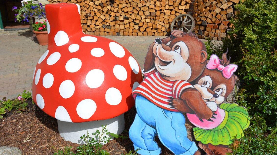 Eine bunte Pilzfigur und zwei niedliche Bärenfiguren stehen im Garten. Die Szenerie ist lebhaft und einladend. | © Märchenwald