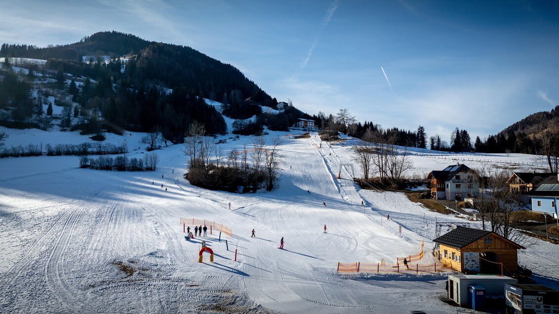 Eine malerische Winterlandschaft mit schneebedeckten Bergen. Auf der Piste sind Skifahrer und eine kleine Hütte ist sichtbar. | © Tourismusverband Murau