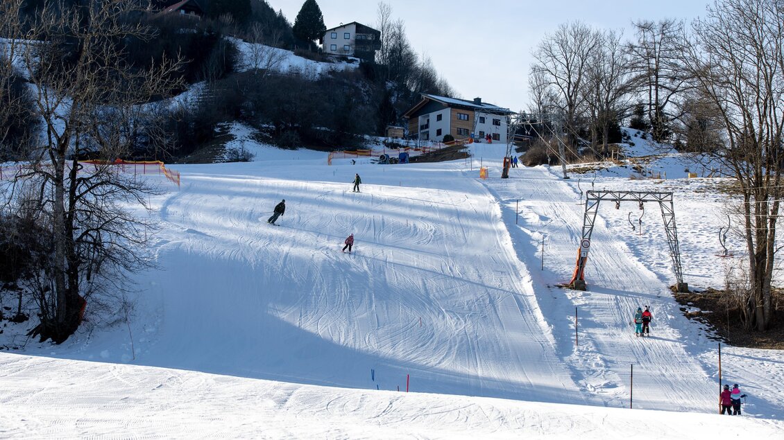 Eine schneebedeckte Piste mit Skifahrern und einem Skilift. Im Hintergrund sind Bäume und Häuser zu sehen. | © Tourismusverband Murau