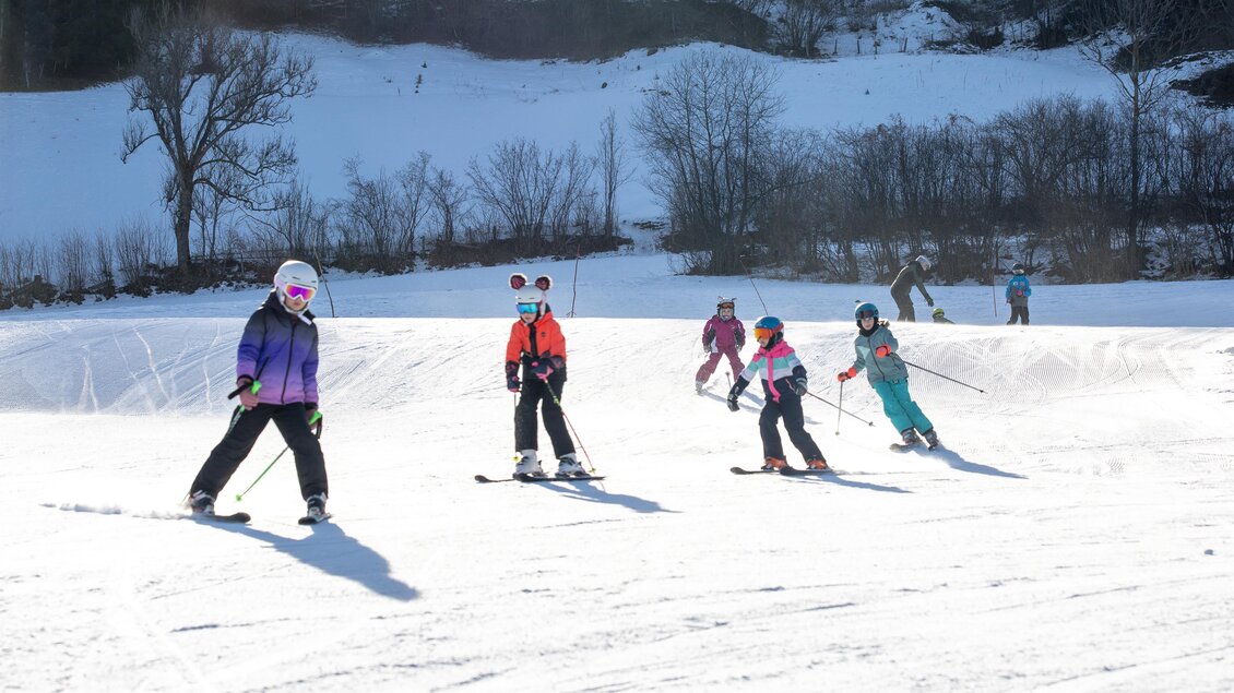Skifahrende Kinder auf einer schneebedeckten Piste bei sonnigem Wetter. Im Hintergrund ist eine verschneite Landschaft zu sehen. | © Tourismusverband Murau