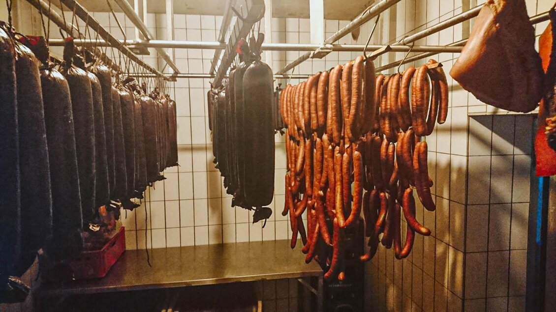 Eine Auswahl von Wurstwaren hängt an einem Gestell in einer Wurstküche. Die Umgebung ist schlicht und funktional gestaltet. | © Seidl