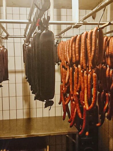 Eine Auswahl von Wurstwaren hängt an einem Gestell in einer Wurstküche. Die Umgebung ist schlicht und funktional gestaltet. | © Seidl