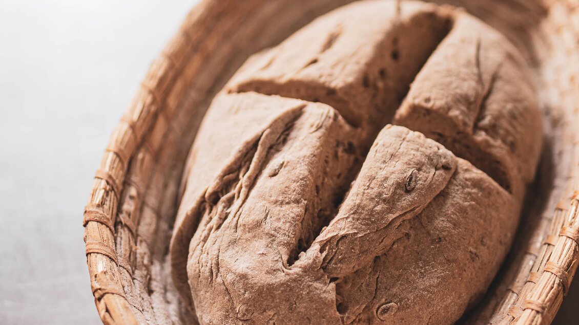 Ein frisch gebackenes Brot liegt in einem rustikalen Korb. Die Oberfläche des Brotes ist leicht rissig und hat eine goldbraune Farbe. | © Anna Ullrich