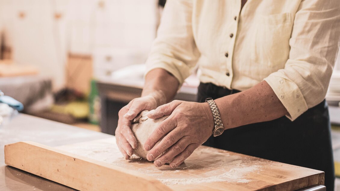Eine Person knetet Teig auf einem Holzbrett. Mehl ist auf der Oberfläche verteilt. | © Anna Ullrich