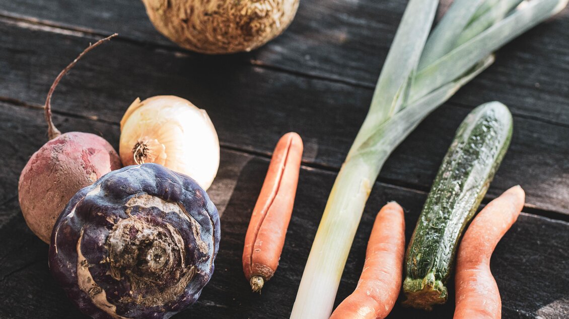 Eine Auswahl frischer Gemüse auf einem Holztisch. Zu sehen sind unter anderem Karotten, Zucchini und Zwiebeln. | © Anna Ullrich