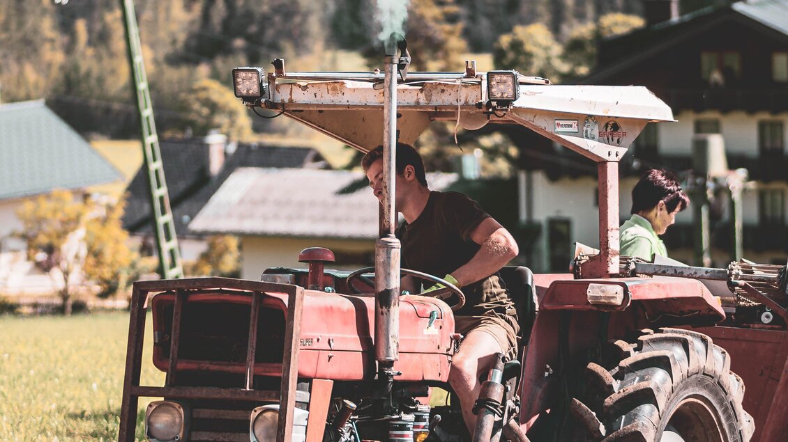 Ein roter Traktor fährt auf einem Feld und stößt grünen Rauch aus. Im Hintergrund sind Häuser und Bäume zu sehen. | © Anna Ullrich