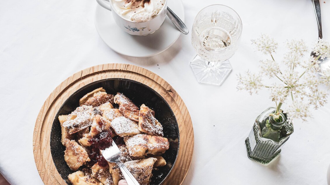 Ein Teller mit warmen, zuckerglasierte Stückchen und einer besonderen Marmelade. Im Hintergrund stehen ein paar Getränke und eine kleine Vase mit Blumen. | © Anna Ullrich