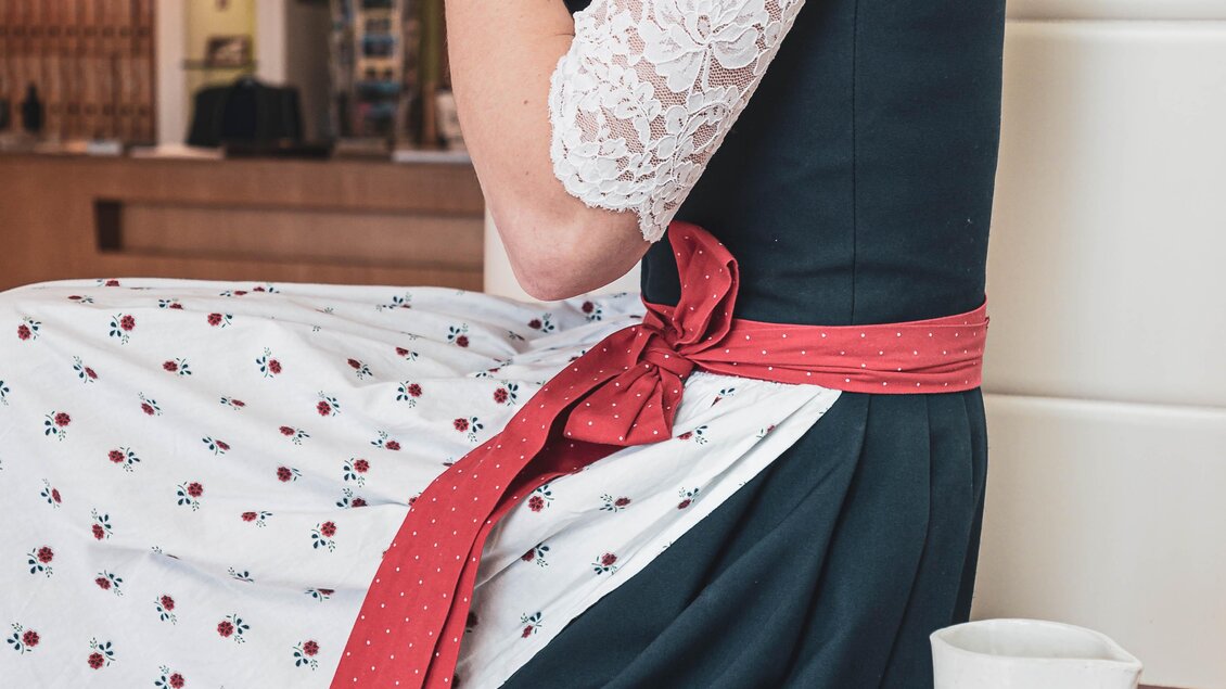 Eine Frau in traditioneller Kleidung sitzt und genießt ein Getränk. Vor ihr liegt ein Teller mit süßen Leckereien. | © Anna Ullrich