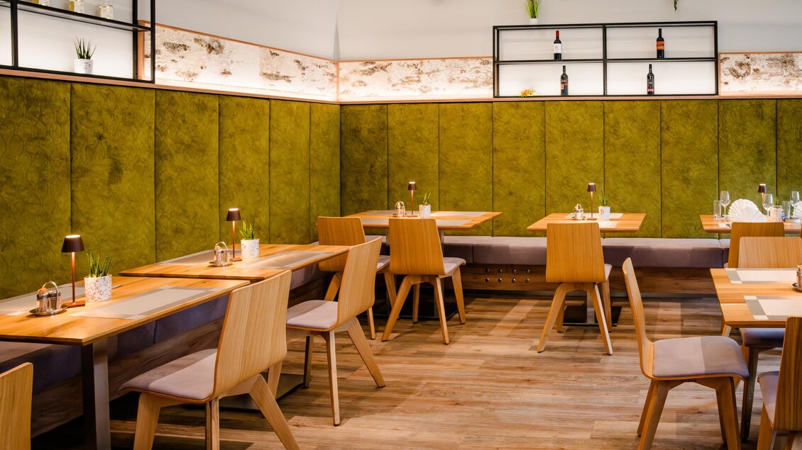 Moderner Gastraum im Feldkirchnerhof mit Holztischen, Stühlen und grüner Wandverkleidung | © Region Graz - Mias Photoart