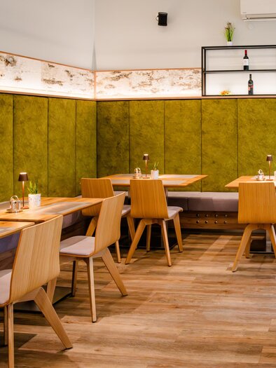 Moderner Gastraum im Feldkirchnerhof mit Holztischen, Stühlen und grüner Wandverkleidung | © Region Graz - Mias Photoart