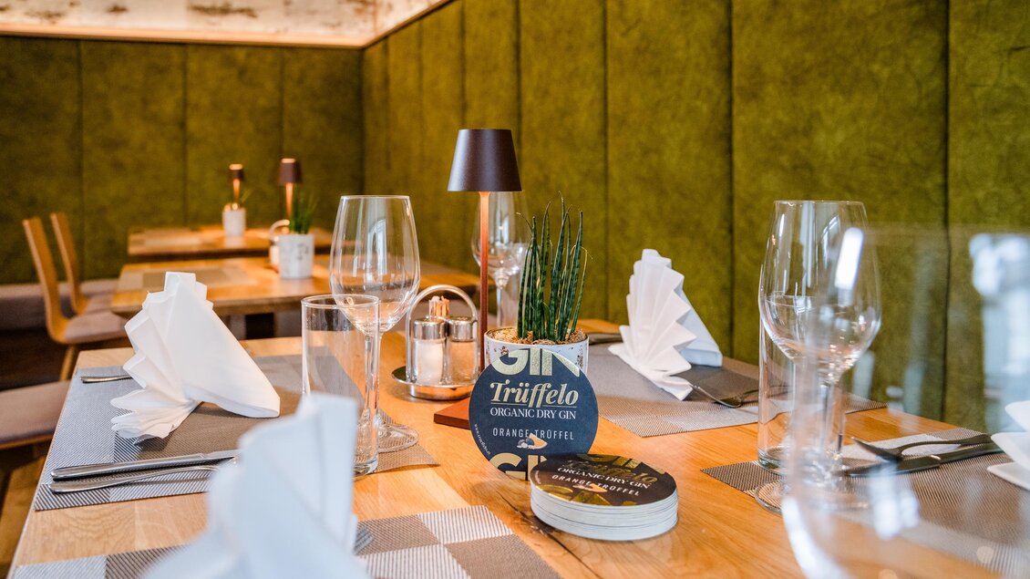 Ein stilvoll gedeckter Tisch in einem Restaurant mit eleganten Gläsern und Servietten. Die Wand ist grün und modern gestaltet. | © Region Graz - Mias Photoart