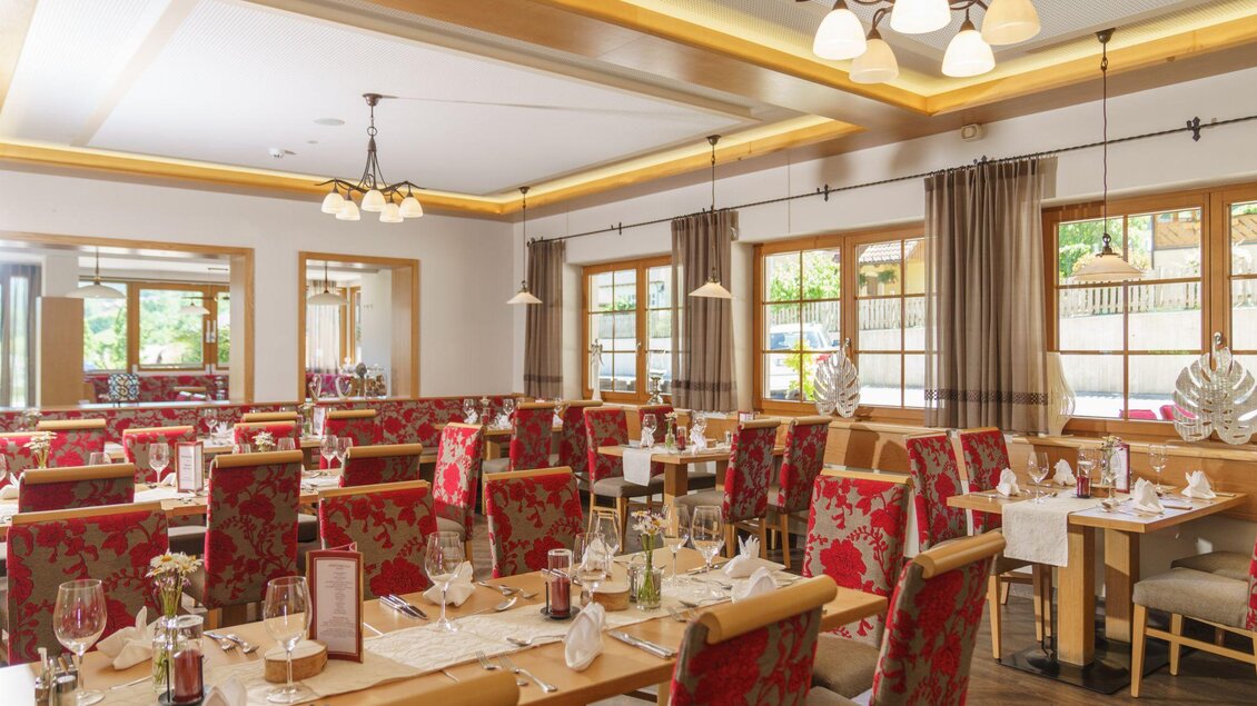 Ein elegantes Restaurant mit holzfarbenen Tischen und roten Stühlen. Große Fenster sorgen für viel Tageslicht und eine einladende Atmosphäre. | © Christine Höflehner