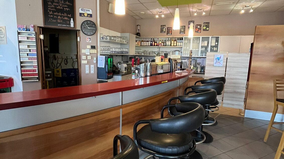 Eine moderne Bar mit einer geschwungenen Theke und schwarzen Barhockern. Die Wände sind hell und freundlich dekoriert, und es gibt verschiedene Getränke im Hintergrund. | © Bettina Fiedler