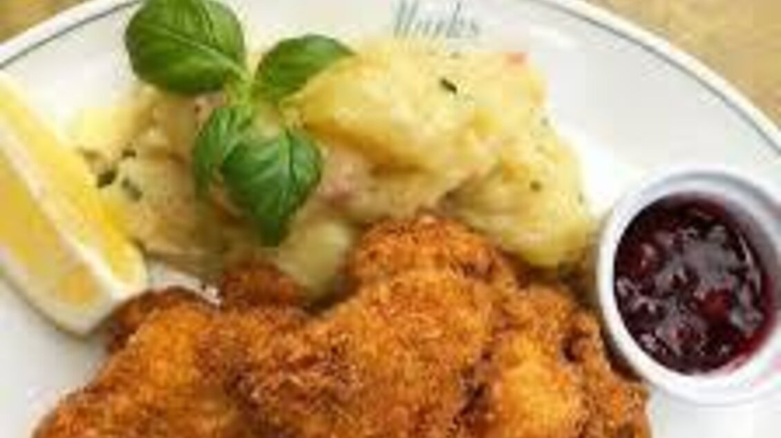 Ein Teller mit knusprigem Hühnchen, Kartoffelbrei und einer Zitronenscheibe. Dazu gibt es eine kleine Schale mit Preiselbeeren. | © Bettina Fiedler