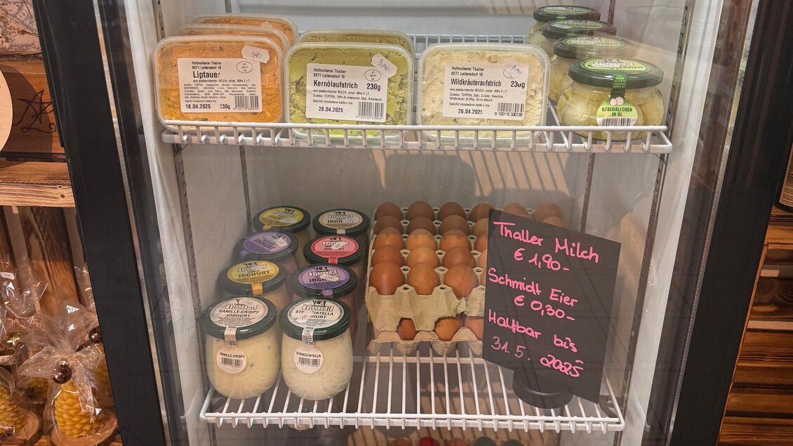 Ein Kühlschrank voller frischer Produkte, darunter Eier, verschiedene Käse und Joghurts. Sichtbare Preise und bunte Marmeladengläser ergänzen das Angebot. | © Sonja Brünner