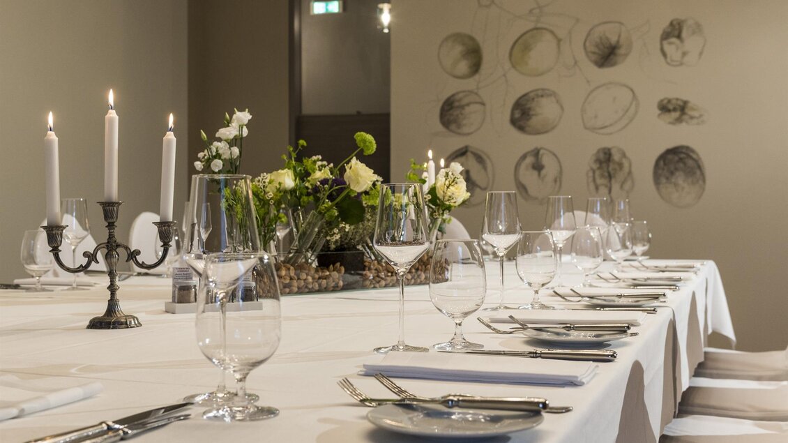 Ein elegant gedeckter Tisch mit Kerzen und Gläsern. Im Hintergrund sind zarte Blumen und dekorative Zeichnungen an der Wand zu sehen. | © Werner Krug