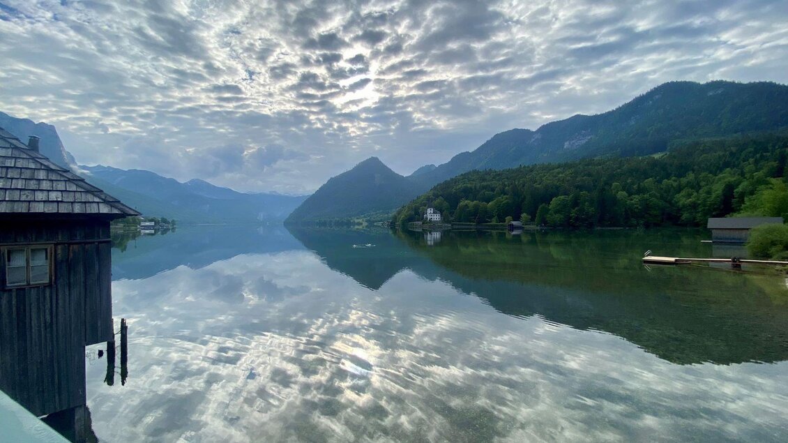 Eine ruhige Seenlandschaft mit Bergen im Hintergrund und einer dramatischen Wolkenbildung. Das Wasser spiegelt die natürliche Schönheit der Umgebung wider. | © Bettina Scheck