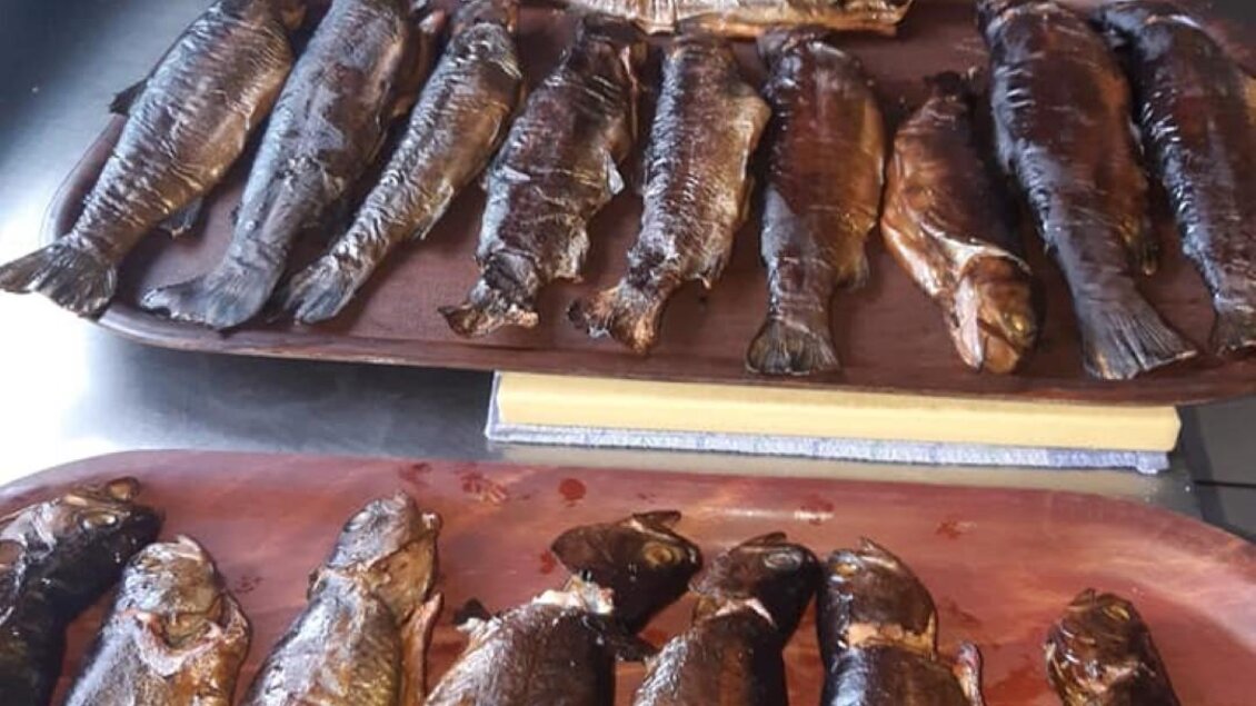 Mehrere geräucherte Fische liegen auf Holzbrettern. Sie sind gleichmäßig angeordnet und zeigen eine glänzende, dunkle Oberfläche. | © Alpengasthof Strutz