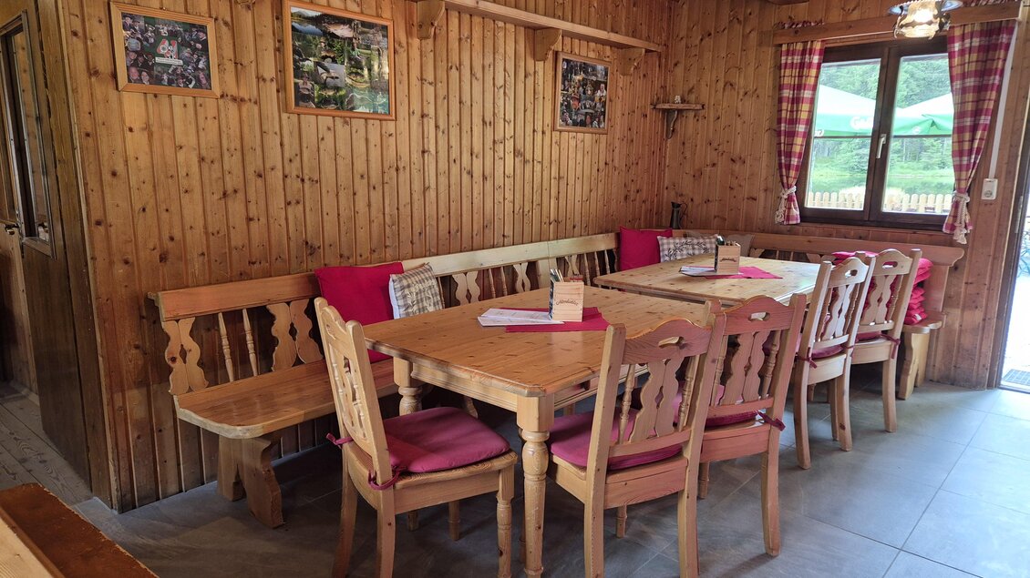 Ein gemütlicher Gastraum mit Holzmöbeln und roten Kissen. Große Fenster lassen viel Licht herein und bieten einen Blick nach draußen. | © TVB Murau