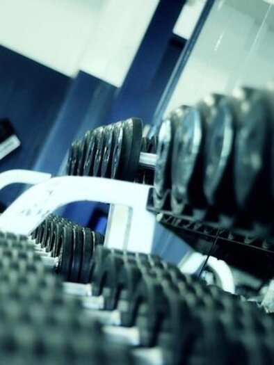 Mehrere Hanteln liegen ordentlich auf einem Ständer in einem Fitnessstudio.
Die schräge Perspektive und die kühlen Farben erzeugen eine moderne, sportliche Atmosphäre.