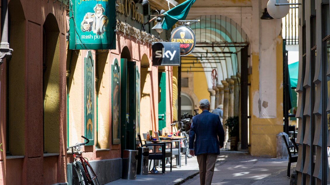 Eine schmale Gasse mit farbenfrohen Fassaden und einem ruhigen Café. Eine Person geht entspannt vorbei, während Fahrräder geparkt sind. | © Graz Tourismus - Harry Schiffer