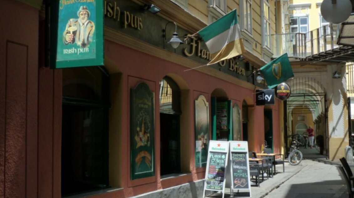 Außenansicht des Flann O'Brien Irish Pubs in einer engen Gasse in Graz, mit irischen Flaggen und Schildern, die das Pub und Angebote bewerben. | © Flann O'Brien