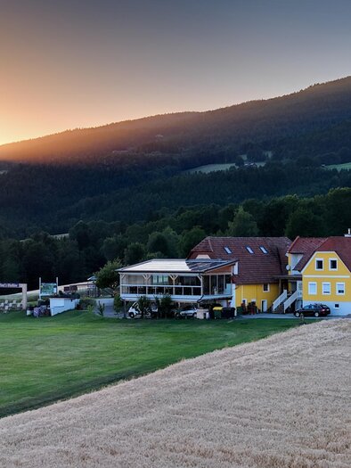 A beautiful country house amid gentle hills. The sun sets behind the mountains, bathing the landscape in warm light. | © Flourl´s Schenke