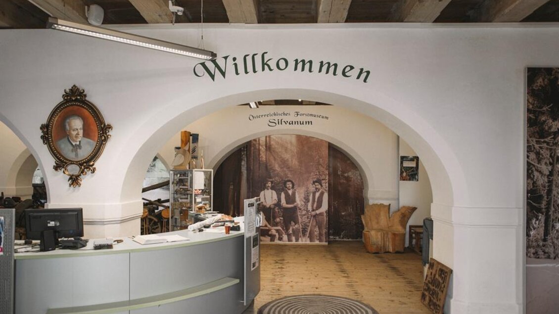 Ein Empfangsbereich mit einem Willkommen-Schild an der Wand. Im Hintergrund sind historische Fotos und eine Holzverkleidung zu sehen. | © Stefan Leitner