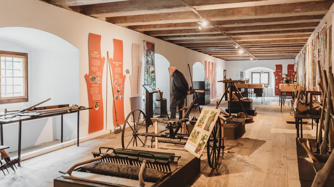 Ein historisches Museum mit landwirtschaftlichen Geräten und Werkzeugen. Im Hintergrund sind informative Ausstellungen und Besucher zu sehen.